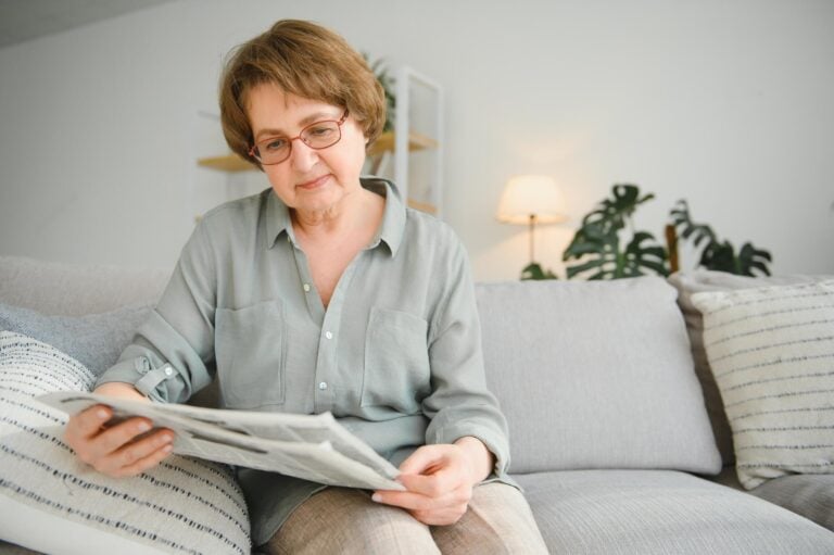 Elderly Woman Reading a Newspaper on Sofa in Assisted Living Facility