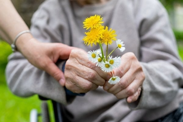 Skilled Nurse Holding Elderly Hands with Flowers during Respite Care
