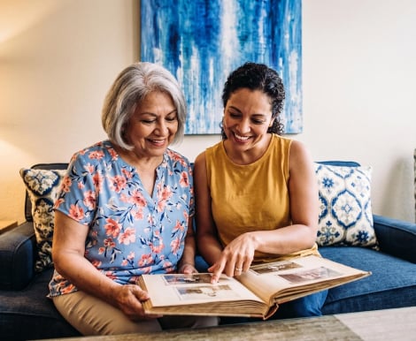 Elderly Woman and Younger Woman Smiling While Browsing a Photo Album at an Assisted Living Community Elderly Woman and Younger Woman Smiling While Browsing a Photo Album at an Assisted Living Community