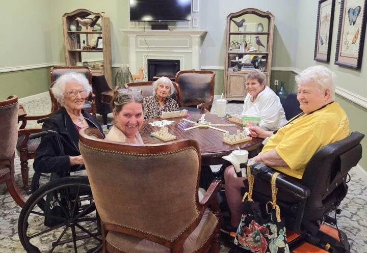 Elderly Women Smiling While Playing Dominoes Around a Table at a Memory Care Community Elderly Women Smiling While Playing Dominoes Around a Table at a Memory Care Community