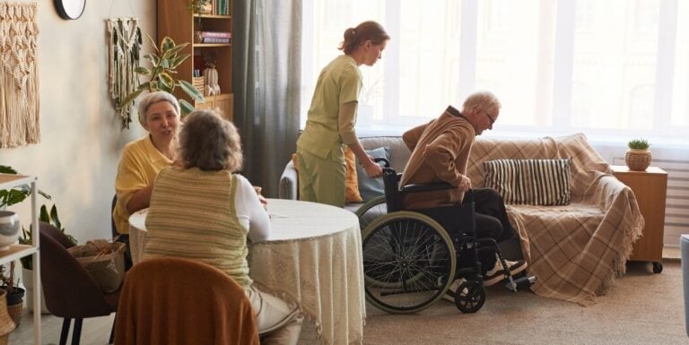 Female Nurse Assisting Elderly Man from Wheelchair at Assisted Living Facility