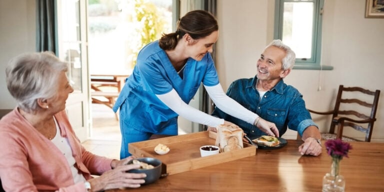 Female Nurse Serving Breakfast to Smiling Elderly Residents at Memory Care Facility
